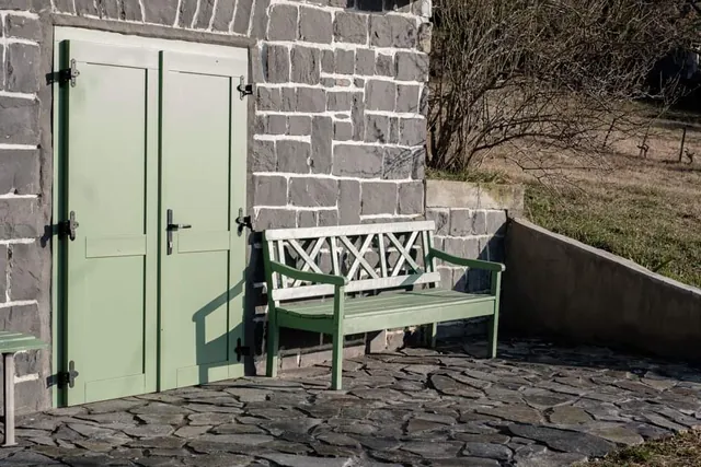 Zöld zsalugáteres ajtó és pad a kőfal előtt